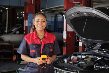 Siyahi bir kadın otomotiv işçisi bakım garajında bir EV araba aküsü ve hibrit motoru kontrol ediyor, uzman elektrikli taşıt servisi ve otomobil sektörünü tamir ediyor..