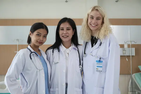 Professional medical staff team, three white uniformed female doctors looking at camera, cheerful and smiling, happy physical work occupation in hospital clinic.