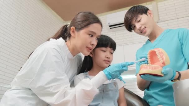 Ασιάτισσα Οδοντίατρος Και Βοηθός Παιδιατρικού Επιδεικνύουν Οδοντόβουρτσα Στο Κοριτσάκι Μοντέλο — Αρχείο Βίντεο