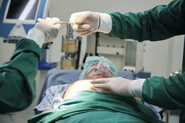 医師が専門の外科医の手にナイフを渡し 病院のIcuで重病患者の手術の準備をします — ストック写真