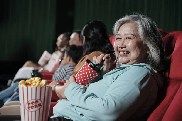 Happy people enjoy watching comedy cinema in movie theaters. Senior Asian woman and audiences have a fun indoor entertainment lifestyle with film art shows and cheerful smiles with drink and popcorn.