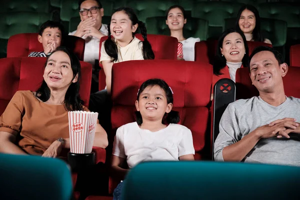 Asian family audience enjoys watching cinema together at movie theaters. Kid and parents have indoor entertainment lifestyle with performance art shows, happy and cheerful with popcorn and a smile.