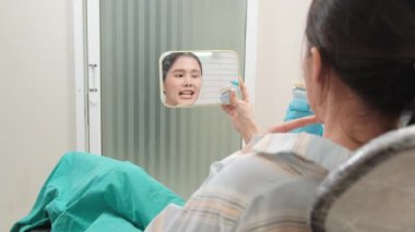 Asyalı erkek diş hekimi diş sağlığı kliniğinde takma diş tonu, diş hijyeni ve hastanede uzman sağlık uzmanı olan genç bir kadına diş bakımı ve beyazlatmayı açıklıyor..