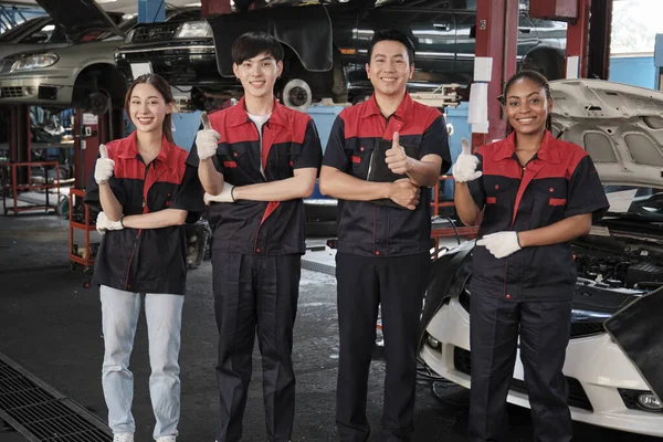 Portrait of multiracial professional mechanic team thumbs up and look at camera, work at car service garage, happy maintenance jobs, check and repair occupation in automotive industry business.