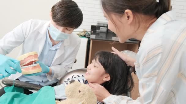 Ασιάτης Παιδιατρικός Οδοντίατρος Επιδεικνύει Οδοντόβουρτσες Ένα Κορίτσι Από Μοντέλο Εμφύτευσης — Αρχείο Βίντεο