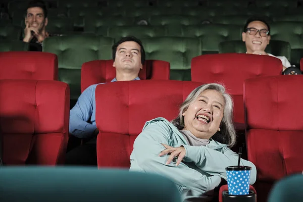Various people enjoy watching comedy cinema in movie theaters. Senior Asian woman and audiences have a fun indoor entertainment lifestyle with film art shows, happy and cheerful with drink and smiles.