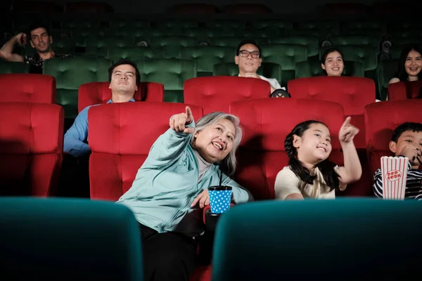 Asian family audiences enjoy watching cinema together at movie theaters. Grandmother and children have indoor entertainment lifestyle with film art shows, happy and cheerful with popcorn and a smile.