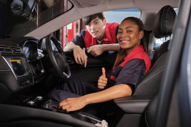 Genç siyahi kadın otomotiv teknisyeni ve ortağı garajın içindeki bakım listesini gülümseyerek kontrol ediyor. Araç servisi tamir ve onarım işleri, endüstriyel meslekler.