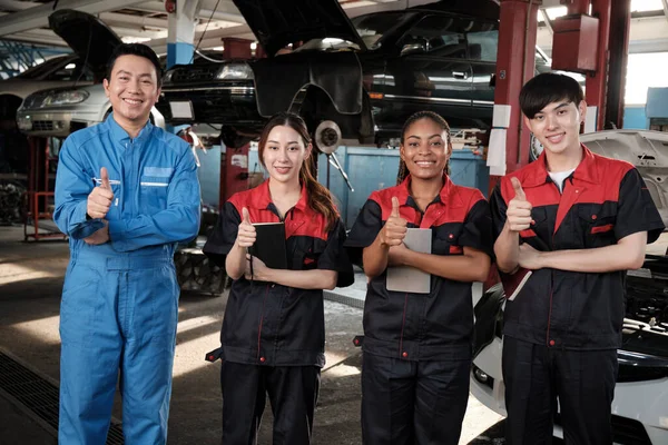 Portrait of multiracial professional mechanic team thumbs up and look at camera, work at car service garage, happy maintenance jobs, check and repair occupation in automotive industry business.