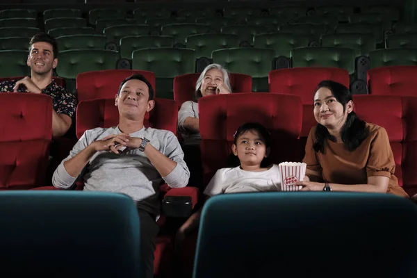 Asian family audience enjoys watching cinema together at movie theaters. Kid and parents have indoor entertainment lifestyle with performance art shows, happy and cheerful with popcorn and a smile.
