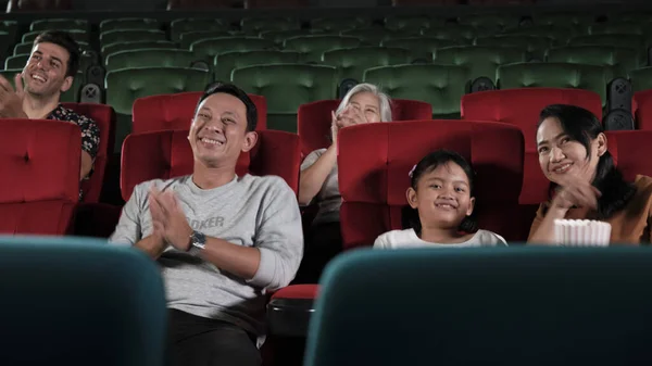 Various people in theater. Asian family, Kid, and parent audiences enjoy watching cinema and applauding together on movie stage, entertainment lifestyle with film art shows, happy and cheerful smiles.