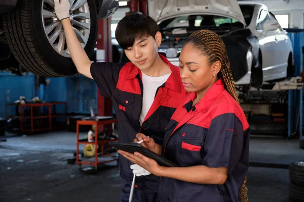Young expert Black female inspects repair checklist with automotive mechanic worker partner, quality suspension technician team at fix garage. Vehicle maintenance service works industry occupation jobs.