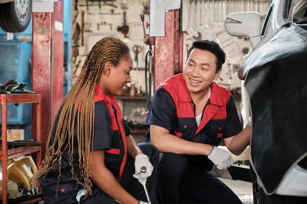 Professional male automotive supervisor trained Black female mechanic technician to screw car wheel nuts for repair at garage, vehicle maintenance service works industry occupation business jobs.