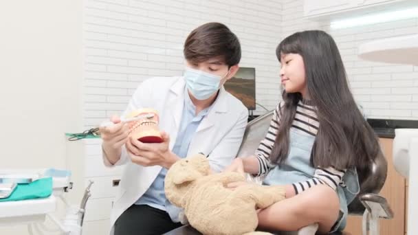 Dentista Asiático Masculino Pediátrico Demonstra Escovas Dentes Para Menina Com — Vídeo de Stock