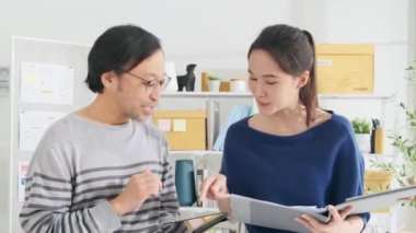 İki genç Asyalı şirket ortağı gelişigüzel küçük işletme ofisinde tartışıp beyin fırtınası yapıyorlar serbest pazarlama işleri, E-ticaret girişimcileri, gelir belgeleriyle birlikte mutlu mesut yaşıyorlar..