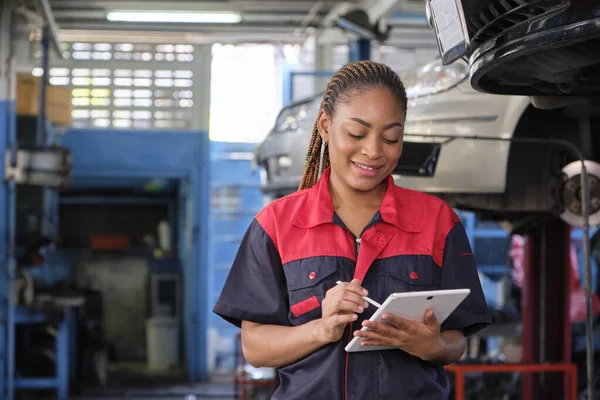 Black female professional mechanic, supervisor engineer, inspects repair work checklists with tablet at garage, service car maintenance, and fixing specialist occupations in auto transport industry.