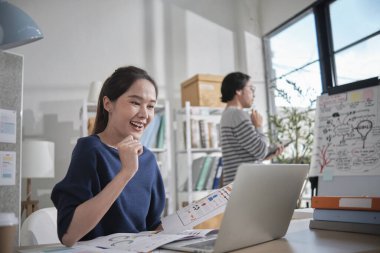 İki genç Asyalı girişimci şirket ortağı, gelişigüzel bir küçük işletme ofisinde, tablet ve dizüstü bilgisayarla çalışan online serbest ticaret girişimcileri ve iş arkadaşları olarak konsantre olup düşünürler..