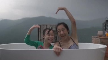 Asyalı aile, anne ve çocuk birlikte takılıyor, küvette rahatça dinleniyor, tatil için doğal manzara seyahat beldesinde tropik dağ manzarası panoramik bir şekilde eğleniyor..