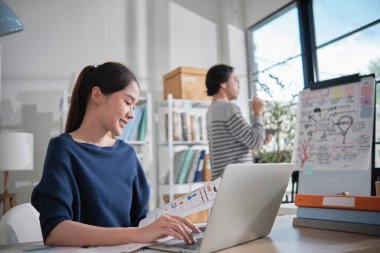 İki genç Asyalı girişimci şirket ortağı, gelişigüzel bir küçük işletme ofisinde, tablet ve dizüstü bilgisayarla çalışan online serbest ticaret girişimcileri ve iş arkadaşları olarak konsantre olup düşünürler..