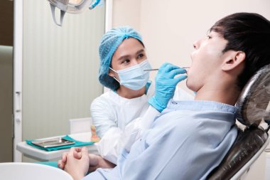 Asyalı kadın diş hekimi genç erkek dişlerini ve diş ağrısı stomatolojisini diş kliniğinde, sağlık kontrollerinde ve doktor muayenehanesinde profesyonel ortodontik sağlık hizmetlerinde inceleyecek..