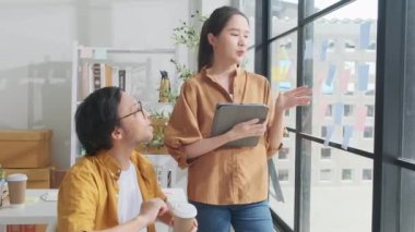 İki genç Asyalı girişim ortağı tartışıyor ve fikir alışverişinde bulunuyor, küçük iş yeri pencerelerinde notlar, pazarlama planlama işleri ve serbest meslek: E-ticaret girişimci iş arkadaşları.
