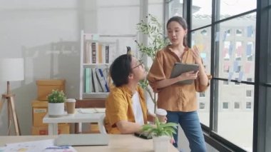 İki genç Asyalı girişim ortağı tartışıyor ve fikir alışverişinde bulunuyor, küçük iş yeri pencerelerinde notlar, pazarlama planlama işleri ve serbest meslek: E-ticaret girişimci iş arkadaşları.