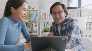 İki genç Asyalı girişim ortağı gelişigüzel küçük işletme ofisinde tartışıyor ve fikir alışverişinde bulunuyor, bir tablet üzerinde pazarlama planlama işleri ve E-ticaret girişimcisi ve iş arkadaşı olarak serbest çalışma.