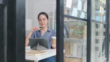 Güzel Asyalı kadın girişimci, günışığı penceresinin yanındaki masasında dijital tabletle çalışmaya odaklanır. Günlük küçük işletme ofisleri, online serbest iş yerleri ve E-ticaret girişimcisi KME.