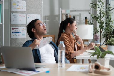 İki Asyalı işçi yaz mevsiminde küçük işletme bürolarında sıcak sıcaklıklarda çalışmaktan memnun değil. Kliması yok, vantilatörlerle rüzgar esiyor, içme suyu içiyor ve terliyor..