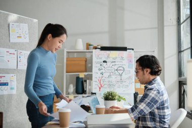 Two young Asian startup company partners discuss and brainstorm in casual small business office, marketing planning ideas, and creatively freelance work as E-commerce entrepreneur and coworker team. clipart