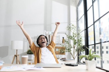 Asyalı erkek serbest çalışan, son teslim tarihi dolduktan sonra yumruklarını kaldırıyor ve rahatlıyor. Günlük küçük işletme bürosunda çalışıyor, bilgisayarla online başlangıç işleri yapıyor, E-ticaret KOBİ 'si tatmin oluyor..