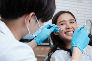 Asyalı erkek diş hekimi, dişçi kliniğinde genç bir bayanın diş stomatolojisini, sağlık kontrollerini ve doktor muayenehanesinde profesyonel diş sağlığı hizmetlerini inceliyor..
