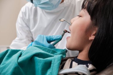 Asyalı kadın pediatrik diş hekimi diş hekiminde Taylandlı bir kızın dişlerini, ağız hijyenini ve bir çocuk hastanesinde profesyonel ortodontik sağlık hizmetlerini kontrol eder ve muayene eder..
