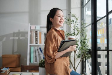 Güzel Asyalı iş kadını portresi, girişim girişimcisi gülümsemesi ve sıradan küçük işletme ofisinin pencerelerine bakması, akıllı pazarlama E-ticaret işleri, mutlu ve neşeli çekici insan..