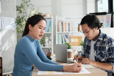 İki genç Asyalı şirket ortağı gelişigüzel küçük işletme ofisinde tartışıyor ve fikir alışverişinde bulunuyor, bir masada pazarlama planlama işleri ve E-ticaret girişimcisi ve iş arkadaşı olarak serbest çalışma.