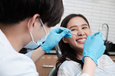 Asyalı erkek diş hekimi, dişçi kliniğinde genç bir bayanın diş stomatolojisini, sağlık kontrollerini ve doktor muayenehanesinde profesyonel diş sağlığı hizmetlerini inceliyor..