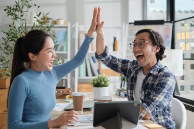 İki Asyalı girişimci birlikte neşeli ve beşlik çakar, webcam aracılığıyla başarılı pazarlama işleri online toplantı, sıradan küçük işletme ofisinde ve E-ticaret iş arkadaşı olarak çalışırlar..