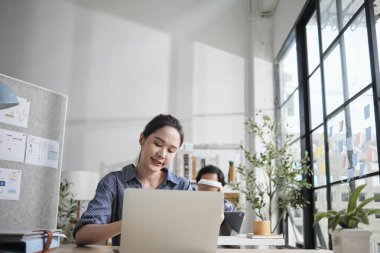 Güzel genç bayan Asyalı işçi çalışmaktan, dizüstü bilgisayar kullanmaktan, masaya gülümsemekten, fikirleri düşünmekten ve günlük ofis ve başlangıç KOBİ 'sinde yaratıcı pazarlama işlerinde yoğunlaşmaktan mutlu..