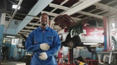 Kendine güvenen zenci erkek tamirci müfettişinin portresi, neşeli işler ve kollar araba tamirhanesinde gülümseme, otomotiv ve taşımacılık sektöründe profesyonel mühendis işleri kontrol etme.