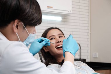 Asyalı erkek diş hekimi, dişçi kliniğinde genç bir bayanın diş stomatolojisini, sağlık kontrollerini ve doktor muayenehanesinde profesyonel diş sağlığı hizmetlerini inceliyor..