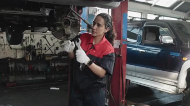 Profesyonel bir İspanyol kadın tamirci otomotiv tekerleklerini kontrol ediyor ve tamir ediyor ve garaj istasyonunda araba süspansiyonları, araç taşımacılığı sektöründe teknisyen mühendisliği hizmetleri sağlıyor..