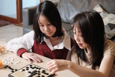 Asyalı aile, anne ve çocuk oyun oynuyorlar Go, dama masasında oyun oynuyorlar sevgi ve neşe dolu, çocuk ve ebeveynin rahatlatıcı hobisi, konsantre olup rekabet ediyorlar..