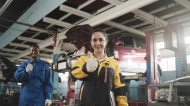 Mutlu profesyonel takım çalışması, Latin kadın müfettiş ve zenci tamirci neşeli, araba tamirhanesinde gülümsemeyle baş parmak, otomotiv sektöründe bakım hizmeti.