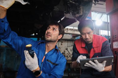 İki erkek tamirci işbirliği yapıyor, Latin ve Asyalı işçiler otomotiv tekerleklerini tamir ediyor ve garaj istasyonunda araba süspansiyonlarını koruyor, ve araç taşımacılığı sektöründe teknisyen mühendisliği hizmeti veriyor..