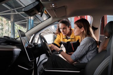 Latin kadın tamirci beyaz müşterili kadına EV araç iç konsol tamir talebi ve araba garantisi, otomotiv garajında müşteri hizmetleri bakımı, ulaşım endüstrisi hakkında açıklama yapıyor..