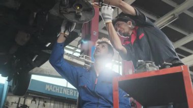 İki erkek tamirci işbirliği yapıyor, Latin ve Asyalı işçiler otomotiv tekerleklerini tamir ediyor ve garaj istasyonunda araba süspansiyonlarını koruyor, ve araç taşımacılığı sektöründe teknisyen mühendisliği hizmeti veriyor..
