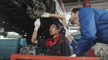 İki erkek tamirci işbirliği yapıyor, Latin ve Asyalı işçiler otomotiv tekerleklerini tamir ediyor ve garaj istasyonunda araba süspansiyonlarını koruyor, ve araç taşımacılığı sektöründe teknisyen mühendisliği hizmeti veriyor..