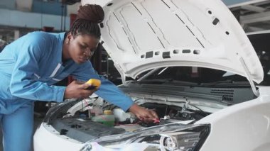 EV araba kontrolü, siyah kadın tamirci sabit otomobil garaj istasyonunda elektrik motoru ve pil hizmetini denetliyor ve koruyor, profesyonel teknoloji taşımacılığı sektörü.