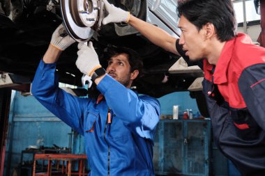 İki erkek tamirci işbirliği yapıyor, Latin ve Asyalı işçiler otomotiv tekerleklerini tamir ediyor ve garaj istasyonunda araba süspansiyonlarını koruyor, ve araç taşımacılığı sektöründe teknisyen mühendisliği hizmeti veriyor..