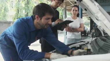 Kadın müşteri ve Asyalı erkek müdür, EV otomobil tamirhanesinde teknisyen motor tamirciliği, akü tamirciliği, müşteri hizmetleri bakımı ve ulaşım sektörü konularında görüştü..